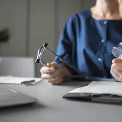 Lekarz z stetoskopem zastanawia się, czy na umowie zlecenie jest L4. Na biurku laptop i dokumenty.