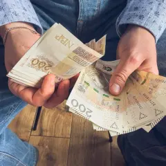 Ręce trzymające stos banknotów 200 zł. To może być wynagrodzenie za urlop, które pozwoli na zasłużony odpoczynek.
