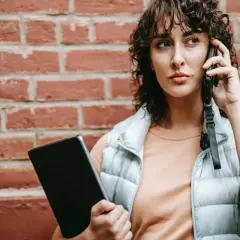 Kobieta rozmawia przez telefon, trzymając tablet. Dyskutuje, czy pracodawca może odmówić urlopu na żądanie.