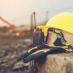 Żółty kask, gogle, rękawice i krótkofalówka na tle budowy.