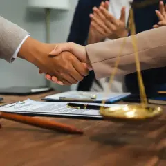 Uścisk dłoni prawników na tle dokumentów i wagi sprawiedliwości. Zastanawiasz się, ile zarabia sędzia sądu rejonowego?