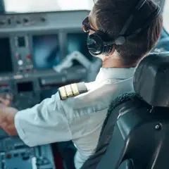 Pilot w kokpicie, słuchawki na uszach, ręce na sterach. Zastanawiasz się, ile zarabia pilot samolotu? To zawód pełen odpowiedzialności i wyzwań.