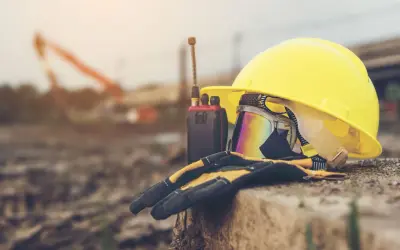 Żółty kask, gogle, rękawice i krótkofalówka na tle budowy.