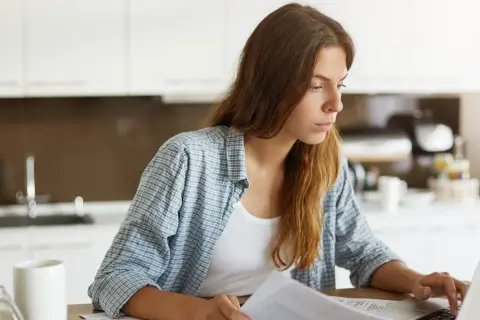 Kobieta pracuje przy laptopie, trzymając dokumenty. Może to być związane z rozliczeniem nip-2.
