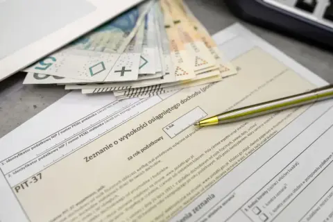 Złożenie PIT-37 z pieniędzmi i długopisem. Zeznanie o wysokości osiągniętego dochodu, pierwszy próg podatkowy.