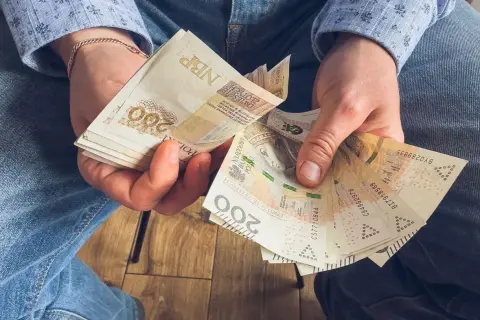 Ręce trzymające stos banknotów 200 zł. To może być wynagrodzenie za urlop, które pozwoli na zasłużony odpoczynek.