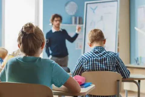 Nauczyciel tłumaczy coś dzieciom w klasie. Zastanawiasz się, ile zarabia nauczyciel klas 1-3?
