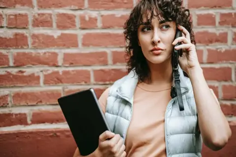 Kobieta rozmawia przez telefon, trzymając tablet. Dyskutuje, czy pracodawca może odmówić urlopu na żądanie.