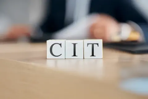 Trzy białe kostki z literami C, I, T ułożone na drewnianym blacie. Temat: podatek CIT.