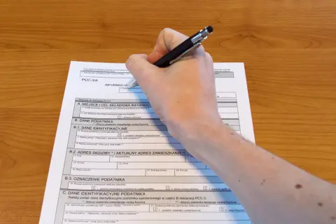 Dłoń pisze na formularzu PCC-3/A, wypełniając dane podatnika.