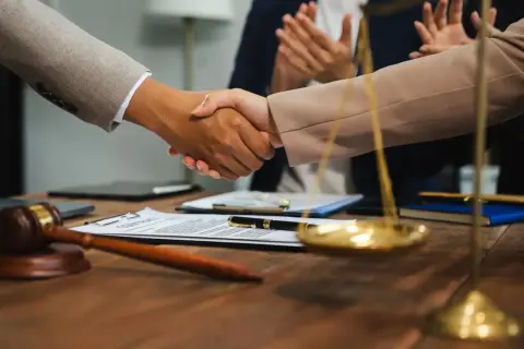 Uścisk dłoni prawników na tle dokumentów i wagi sprawiedliwości. Zastanawiasz się, ile zarabia sędzia sądu rejonowego?