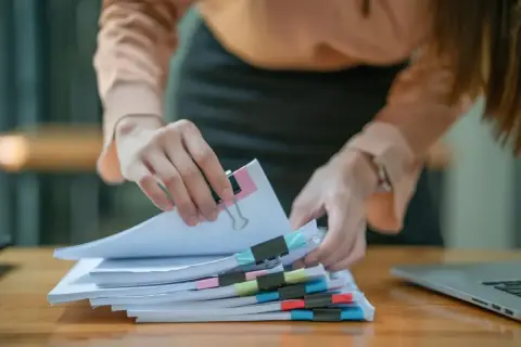 Ręce sortują dokumenty z kolorowymi spinaczami. Czy to rachunki, czy może coś związanego z fiskusem?