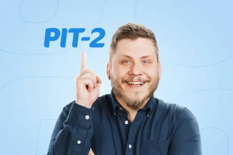 Uśmiechnięty mężczyzna w granatowej koszuli wskazuje palcem na napis PIT-2.