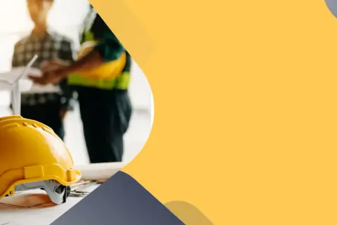 Żółty kask budowlany na planach. W tle zespół inżynierów, w tym cieśla szalunkowy, omawia projekt.