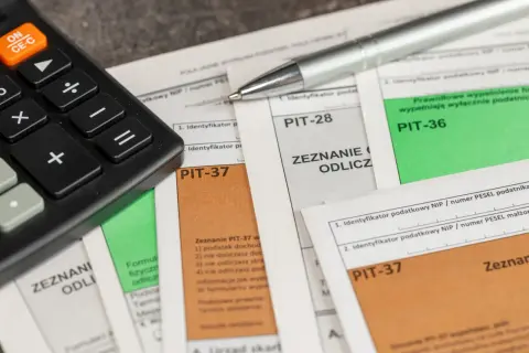 Kalkulator i długopis leżą na dokumentach PIT-28, PIT-36 i PIT-37. Czas na rozliczenie podatku!
