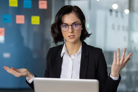 Kobieta w okularach, ubrana w czarną marynarkę, gestykuluje, tłumacząc coś przy laptopie. Na szklanej ścianie w tle widać kolorowe karteczki, jakby z pomysłami na ip box.
