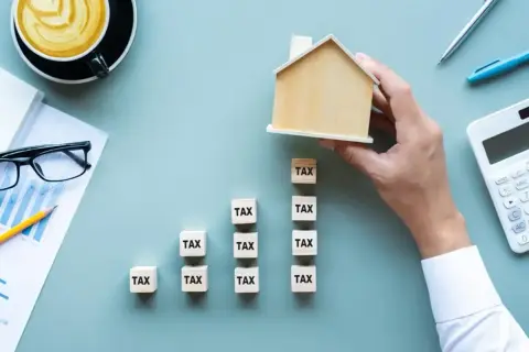 Klocki z napisem "TAX" tworzą rosnący wykres, a dłoń kładzie na szczycie domek. Zastanawiasz się, do kiedy trzeba zapłacić podatek?