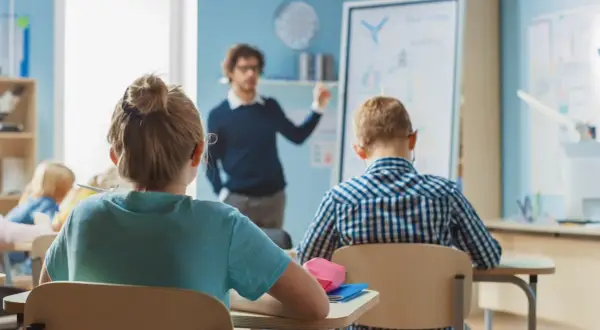 Nauczyciel tłumaczy coś dzieciom w klasie. Zastanawiasz się, ile zarabia nauczyciel klas 1-3?