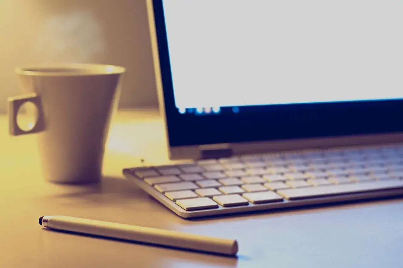 Kawa, laptop i rysik na biurku. Idealne warunki, by zastanowić się, jak zakończyć maila.