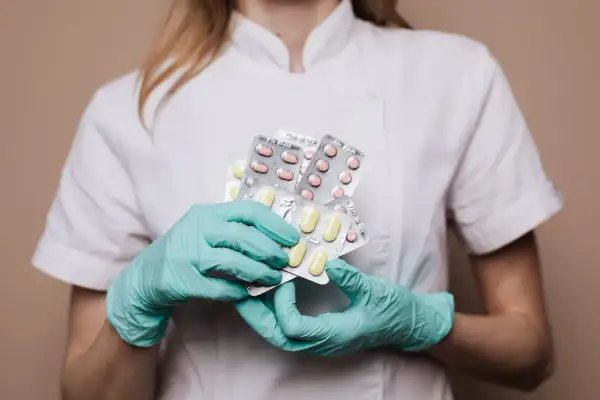 Farmaceuta w rękawiczkach trzyma kilka opakowań tabletek.