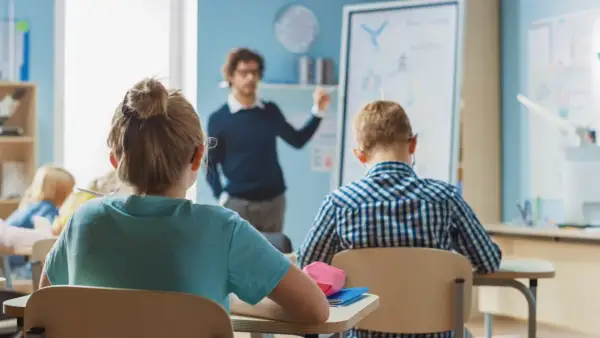 Nauczyciel tłumaczy coś dzieciom w klasie. Zastanawiasz się, ile zarabia nauczyciel klas 1-3?