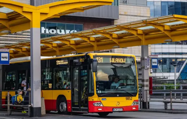 Kierowca autobusu linii 131 dojeżdża do przystanku Wilanów. Żółto-czerwony pojazd czeka na pasażerów pod żółtą wiatą.