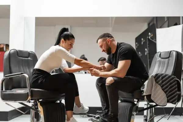 Barber w czarnym t-shircie i podartych jeansach siedzi na fotelu, trzymając dłoń klientki. Zastanawia się, ile zarabia barber.