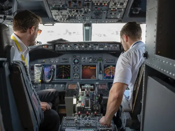 Dwóch pilotów samolotu w kokpicie. Jeden z nich, pilot, patrzy na instrumenty, drugi obsługuje sterowanie.